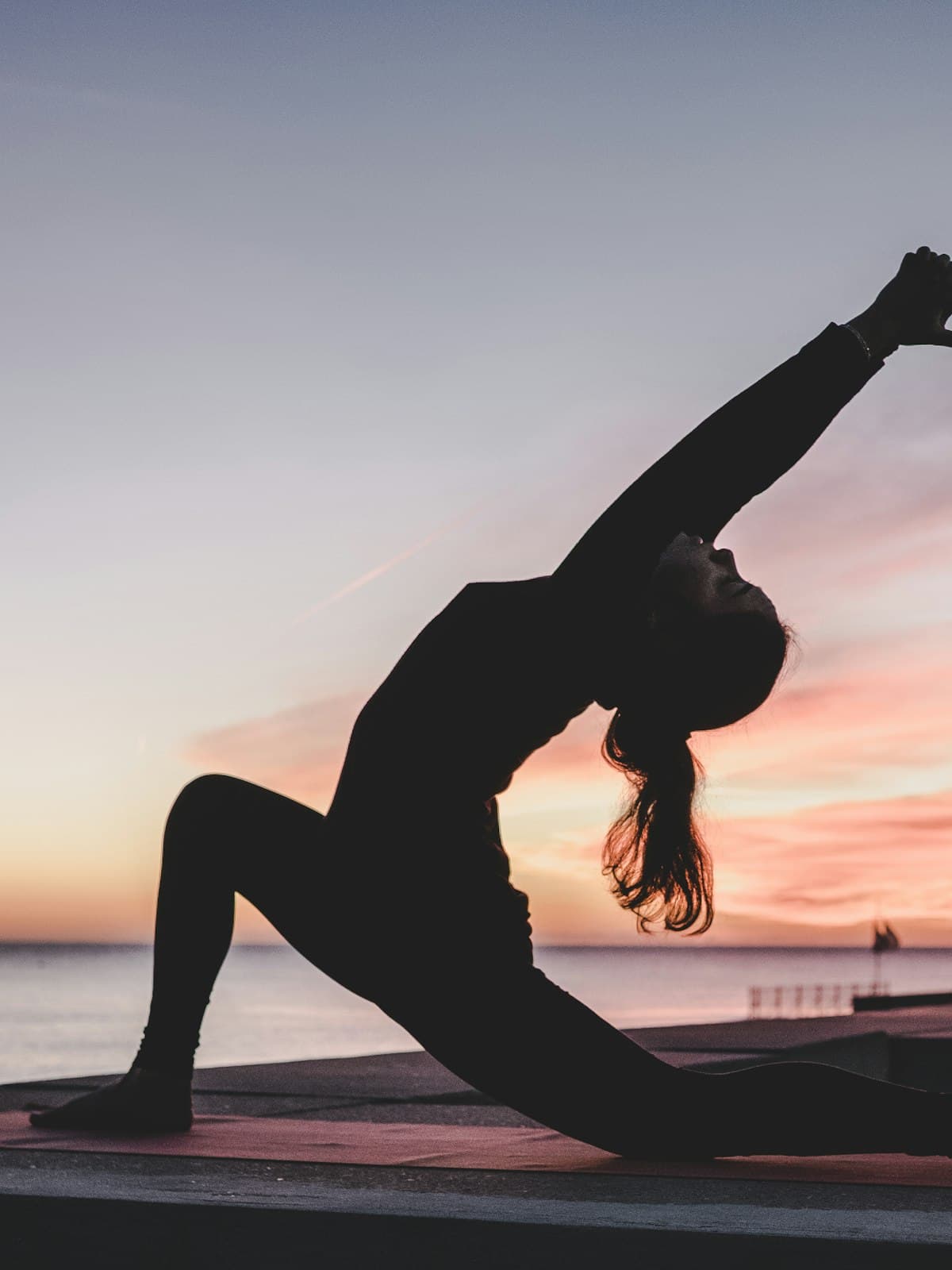 Person practicing yoga beside the ocean at sunrise