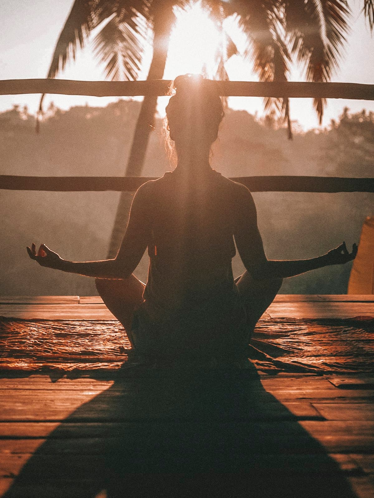 Silhouette of a person meditating at sunrise on a wooden deck